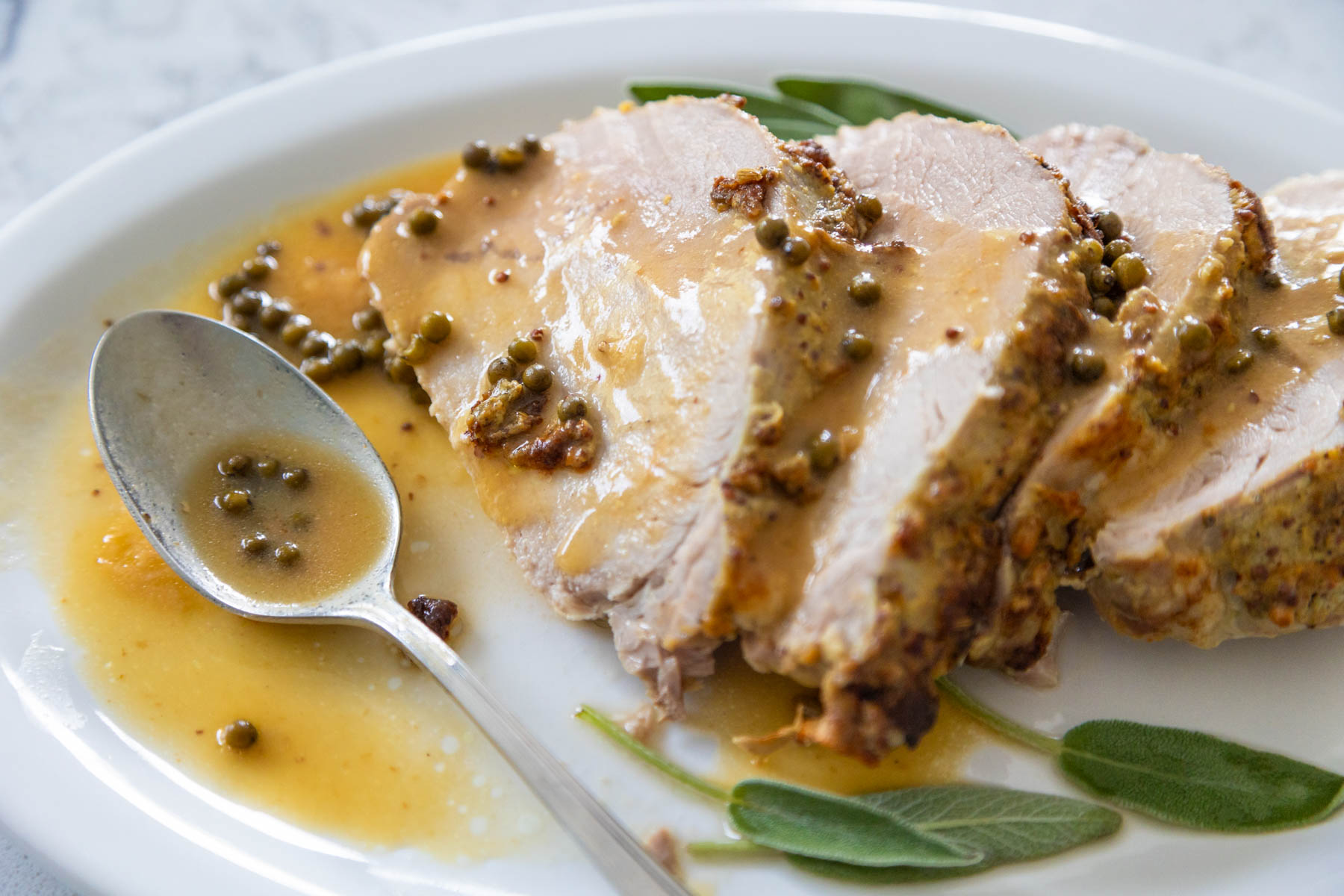 The platter has several slices of pork with a spoon filled with peppercorn sauce.