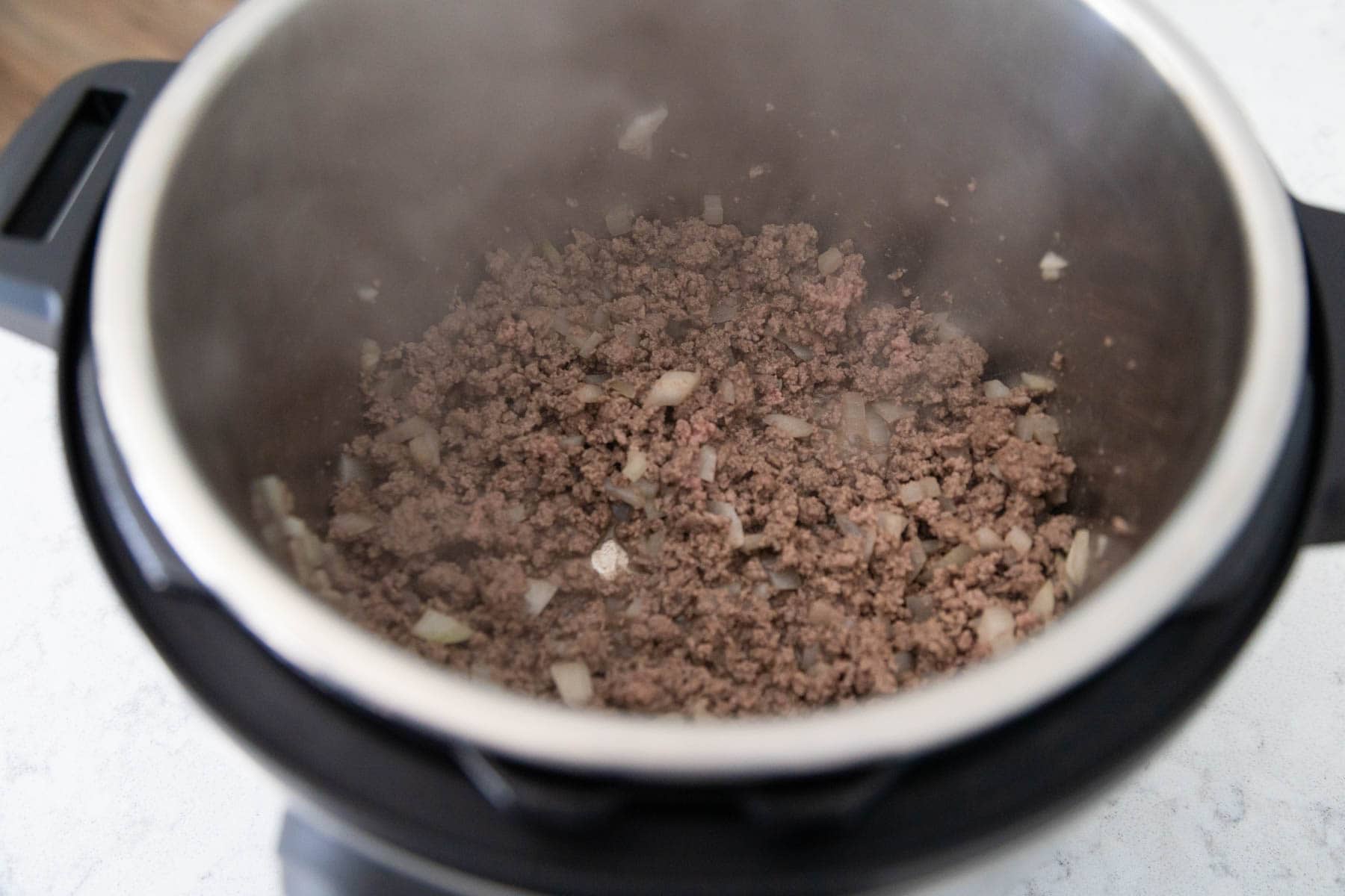 The ground beef and chopped onions are cooking in the Instant Pot on the Saute function.