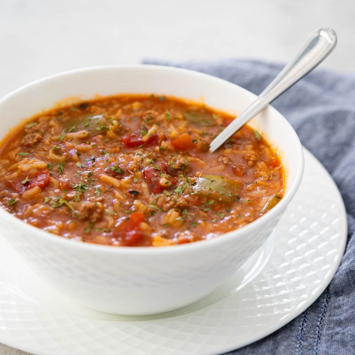 A white bowl with a spoon is filled with the tomato-based stuffed pepper soup.