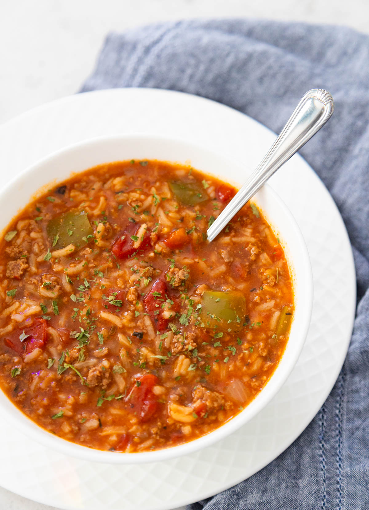 A bowl of tomato-based stuffed pepper soup has rice, chunks of bell peppers, and ground beef floating in the broth.