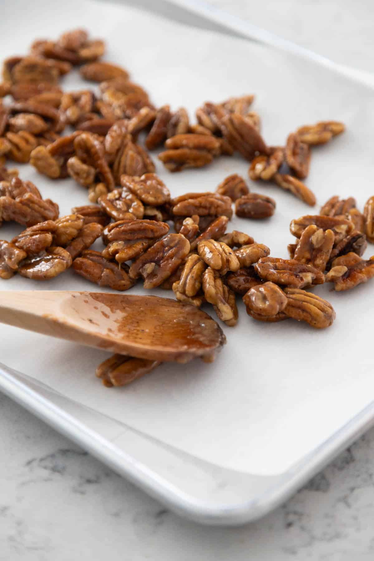 The pecans are being spread apart on the baking pan lined with parchment.