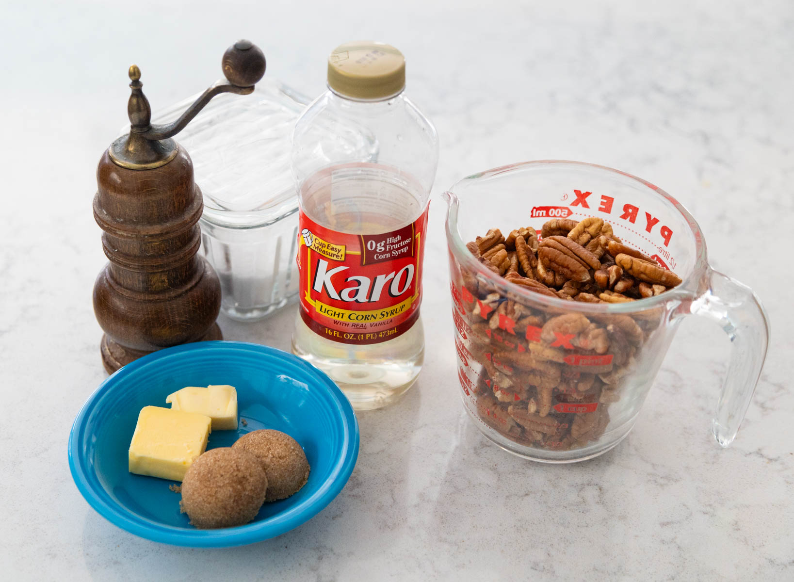 The cup of pecans is on the counter next to the rest of the ingredients used to make the glaze.