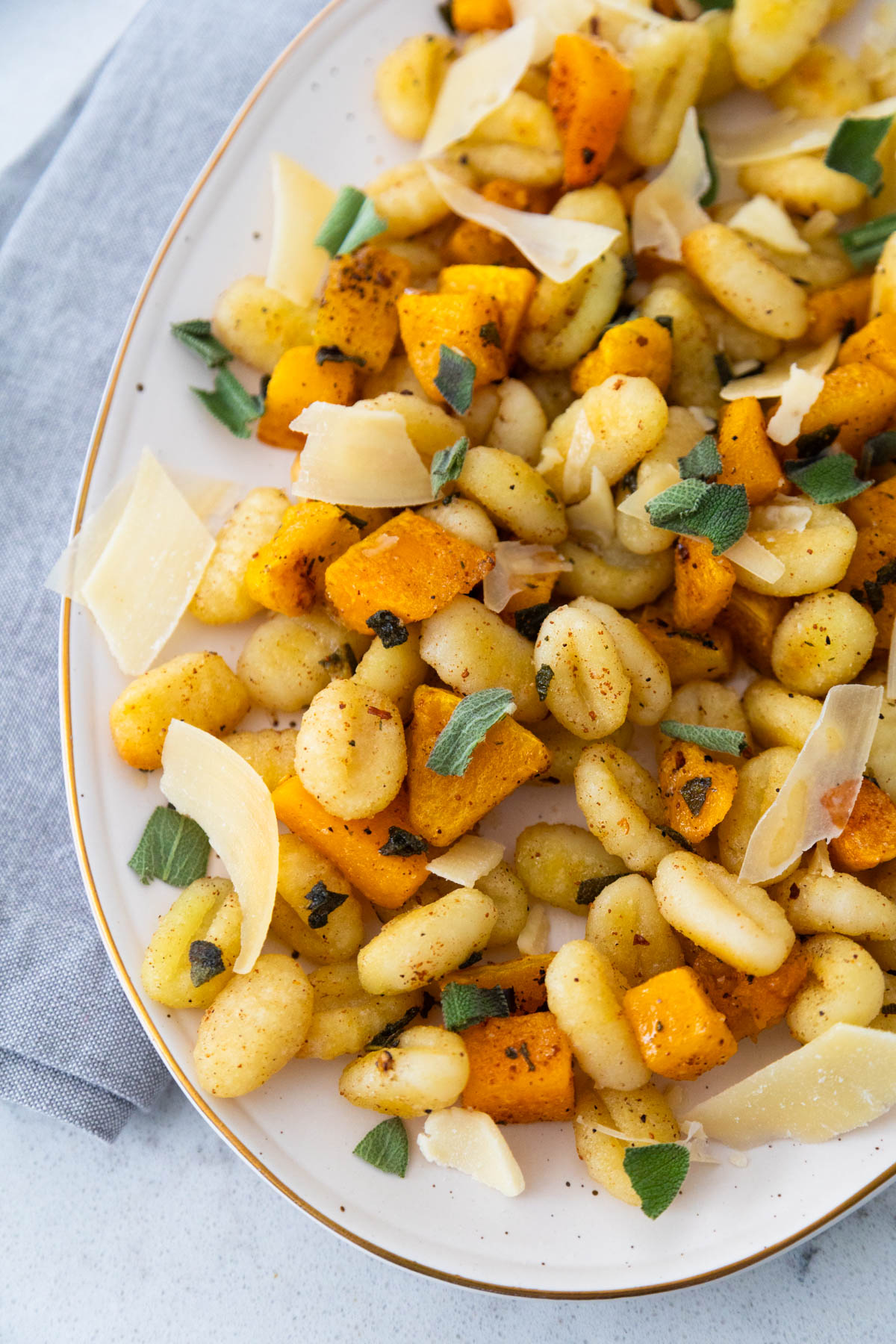 A platter is filled with roasted gnocchi and butternut squash with parmesan shavings and fresh sage leaves ripped and sprinkled over the top.