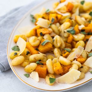 A platter filled with roasted gnocchi, butternut squash, and parmesan cheese shavings with ripped fresh sage sprinkled over the top.