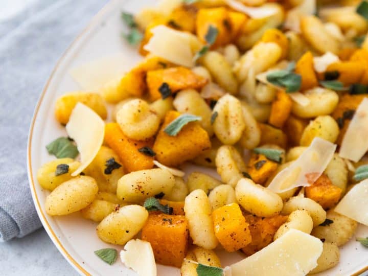 A platter filled with roasted gnocchi, butternut squash, and parmesan cheese shavings with ripped fresh sage sprinkled over the top.