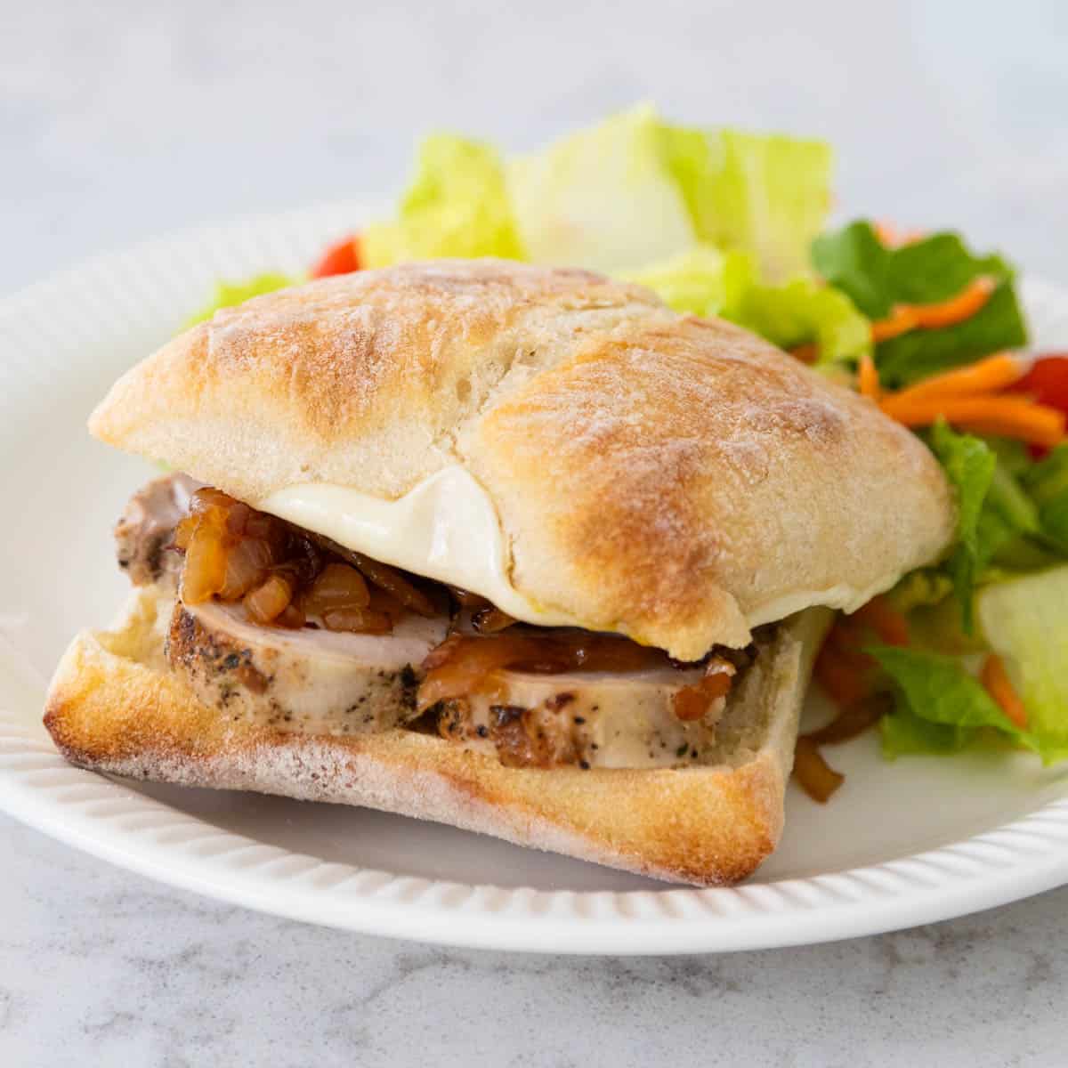 The roasted pork sandwich is on a white plate next to a side salad.