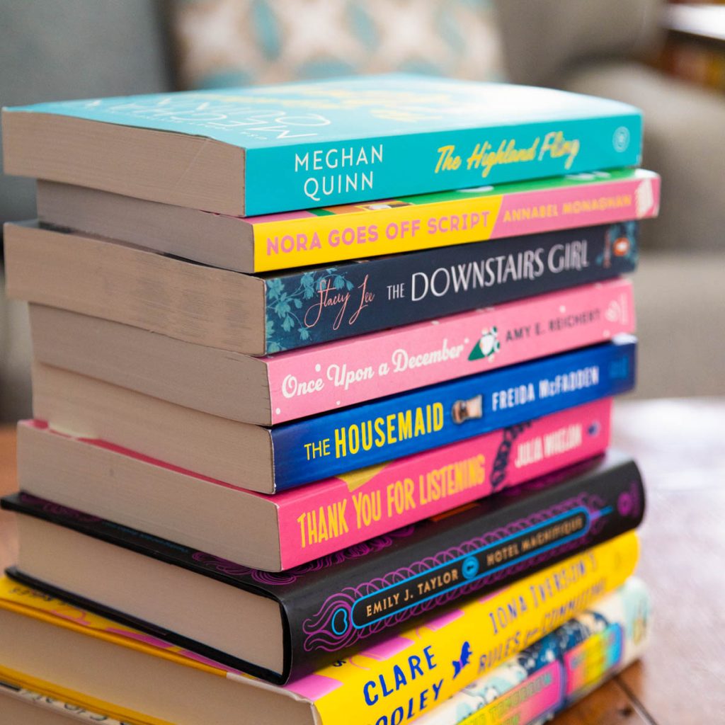 A stack of colorful books for women are sitting in a stack on the coffee table in front of a couch.