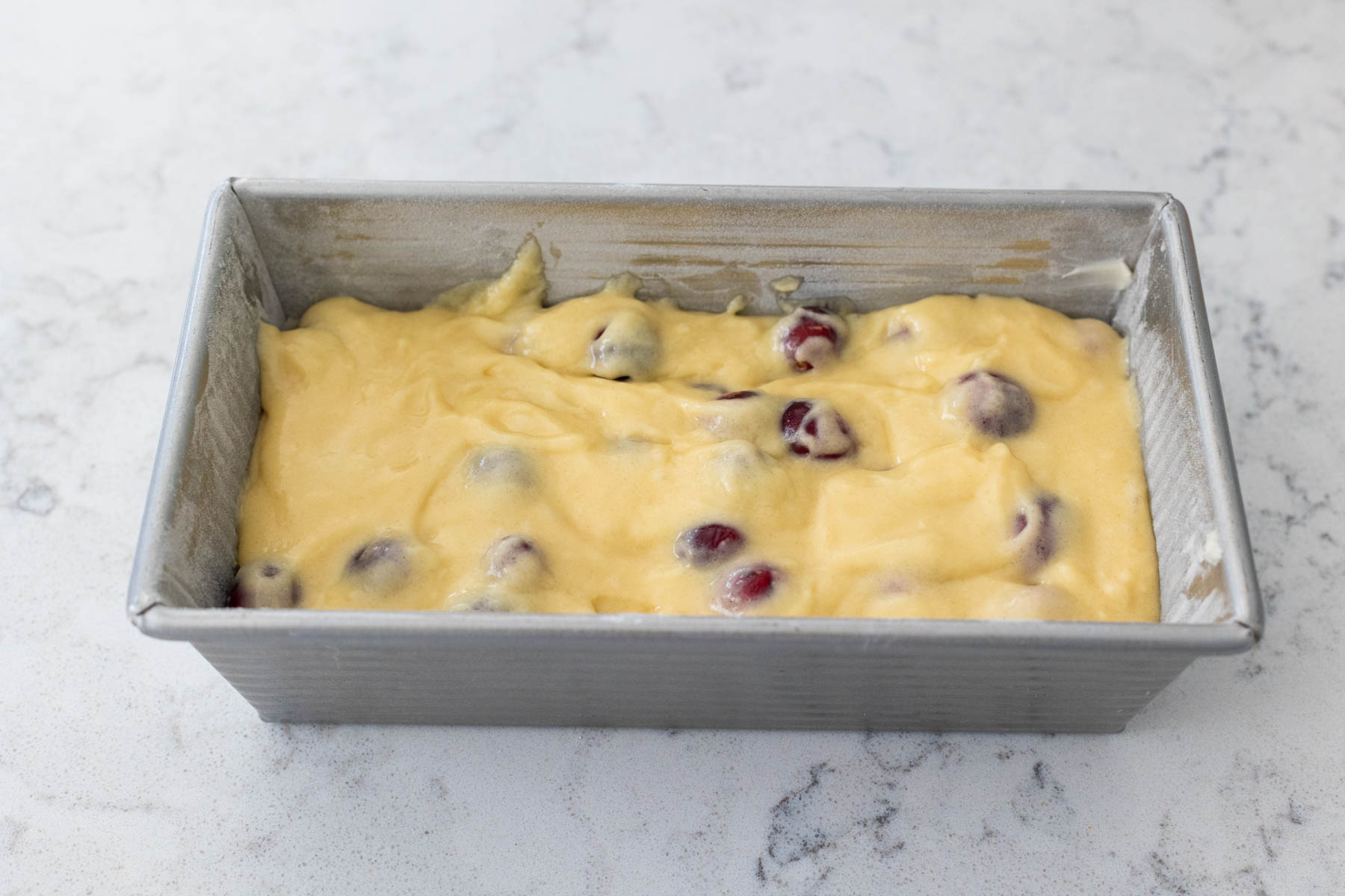 The cranberry bread batter has been leveled into a bread pan.