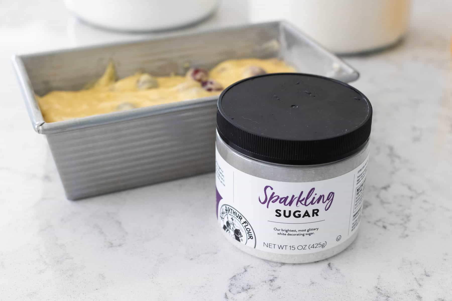 A container of King Arthur Baking's sparkling sugar sits on the counter in front of the quick bread pan.