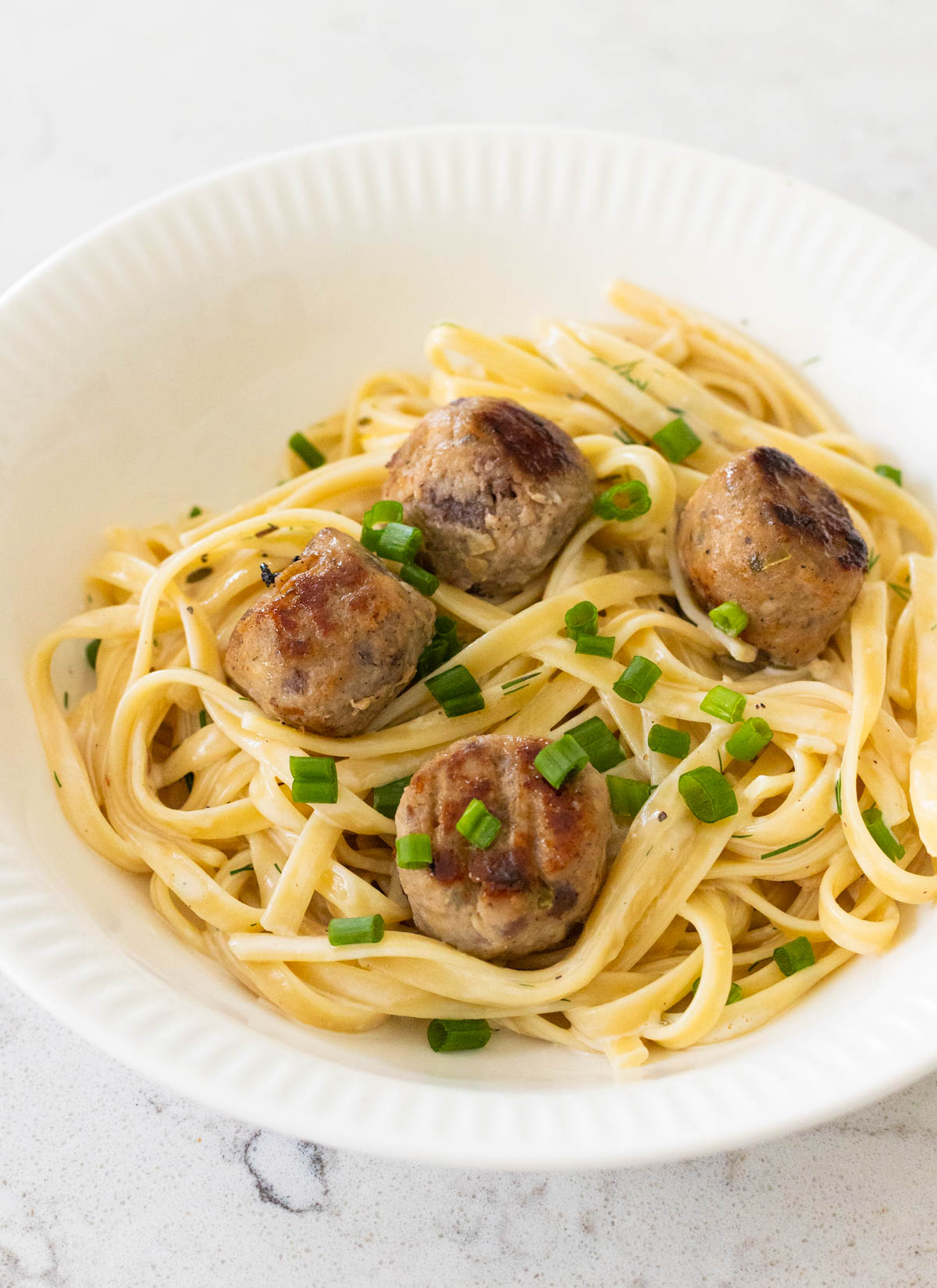 A bowl of pasta is topped with four cranberry jalapeño meatballs.