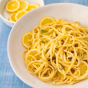 A white bowl is filled with creamy lemon garlic pasta with fresh dill and lemon slices for garnish.