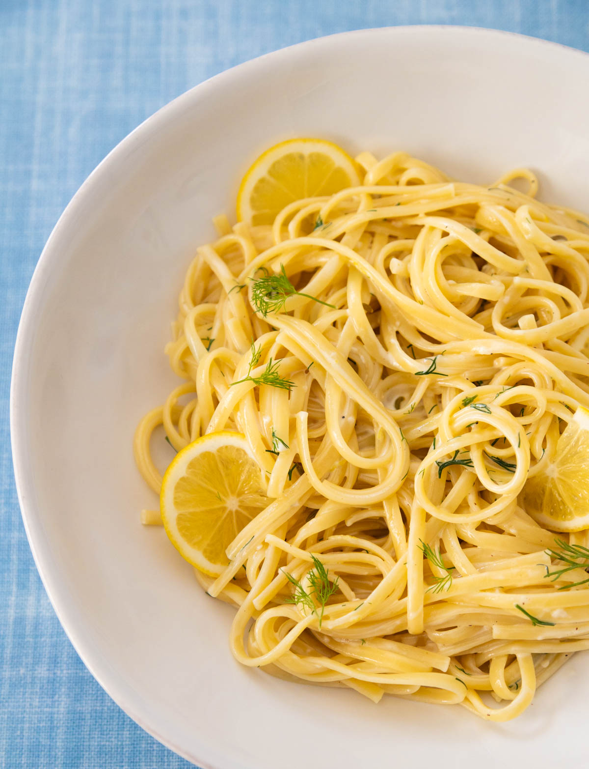 The bowl filled with creamy lemon garlic pasta has fresh dill for garnish and a few sliced lemons on the side.