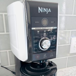 A ninja creami appliance sits on the kitchen counter next to the tiled backsplash.