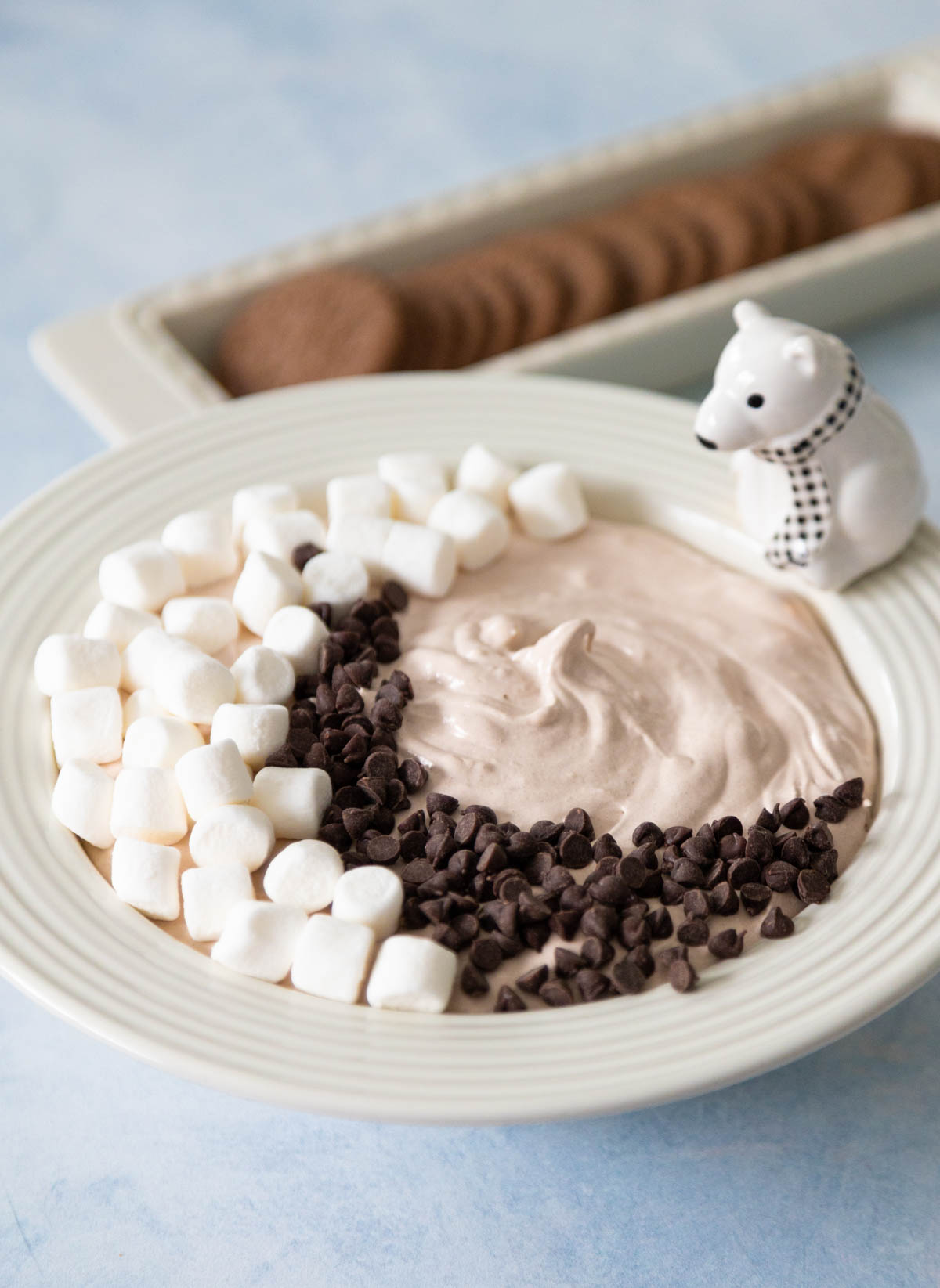 The dip has been garnished with marshmallows and chocolate chips. A platter of chocolate wafer cookies sits next to the bowl.
