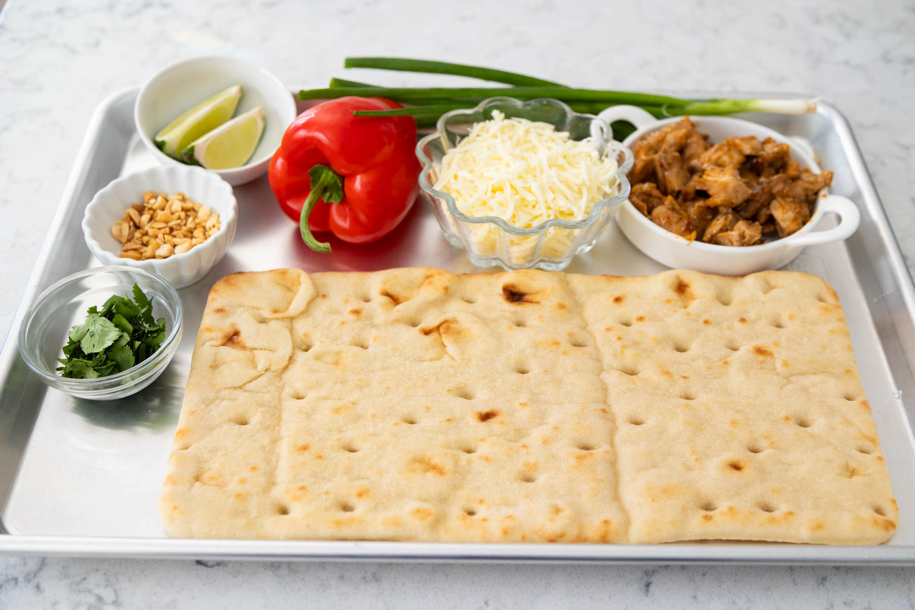 The ingredients to make the Thai chicken pizza are on a baking sheet.