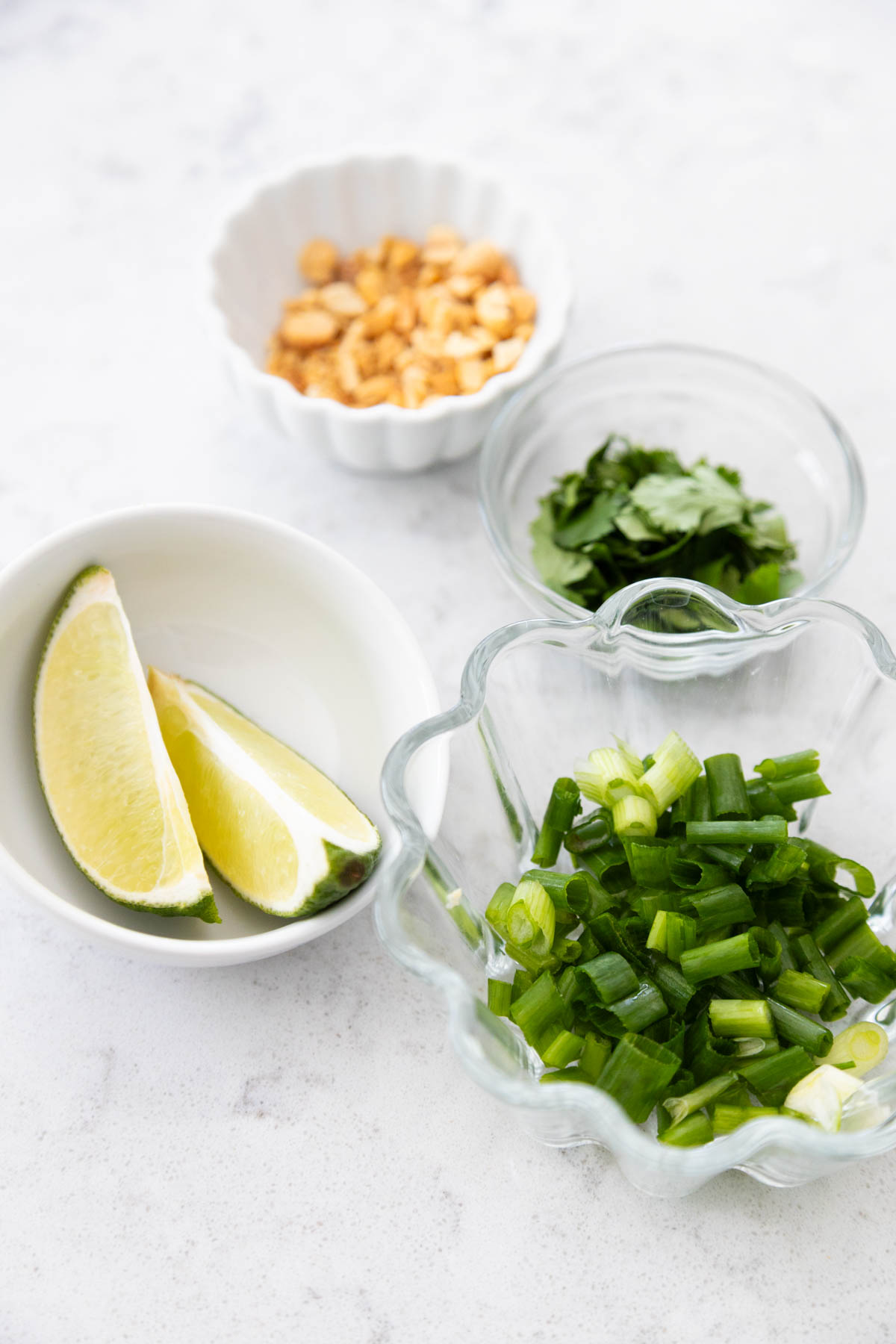 The limes, green onions, chopped peanuts, and cilantro are prepped in small bowls.