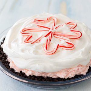 A candy cane pie with Oreo cookie crust, pink peppermint filling, and white Cool Whip on top has a snowflake design made out of mini candy canes on top.