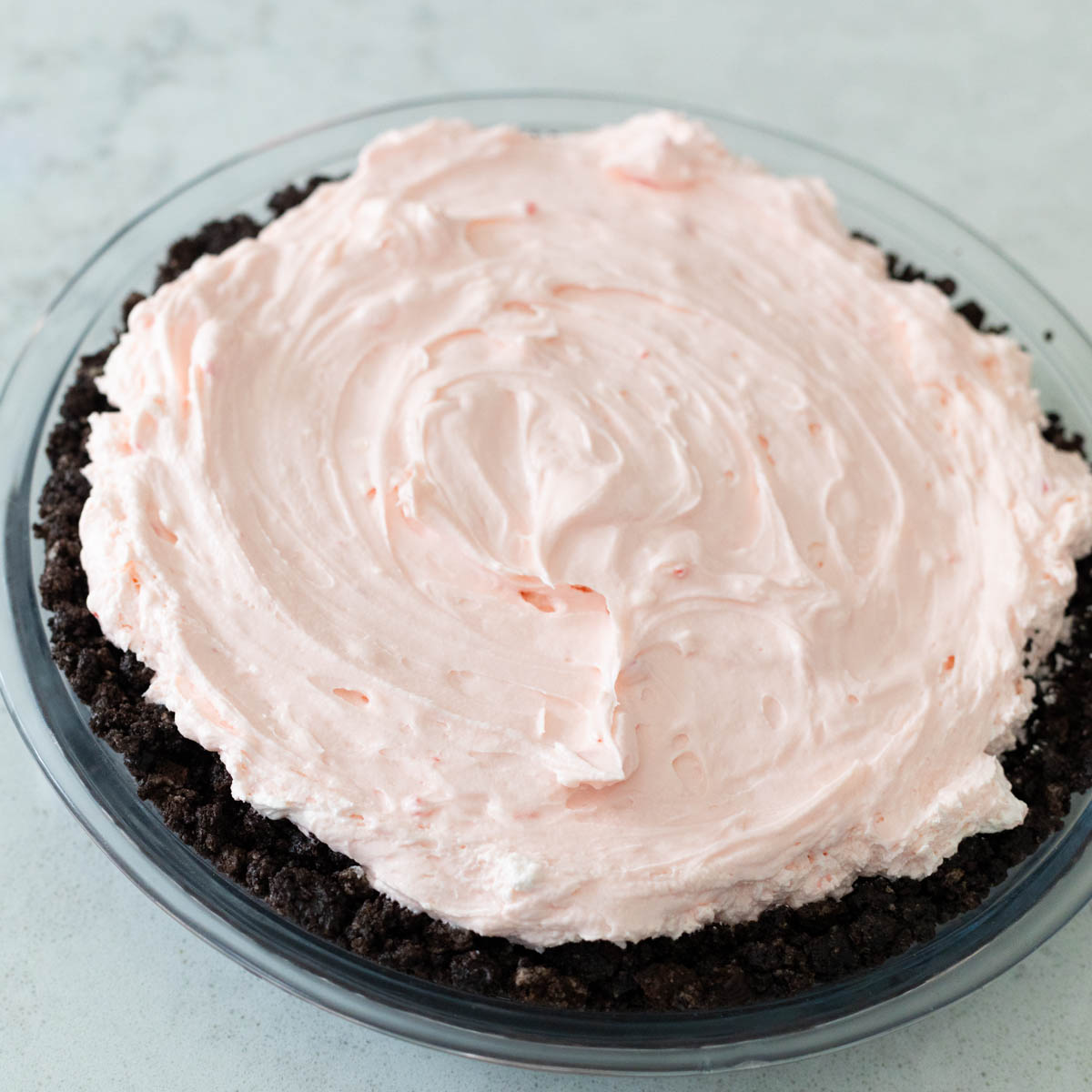 The light pink, fluffy peppermint pie filling has been smoothed into the prepared chocolate Oreo cookie crust.