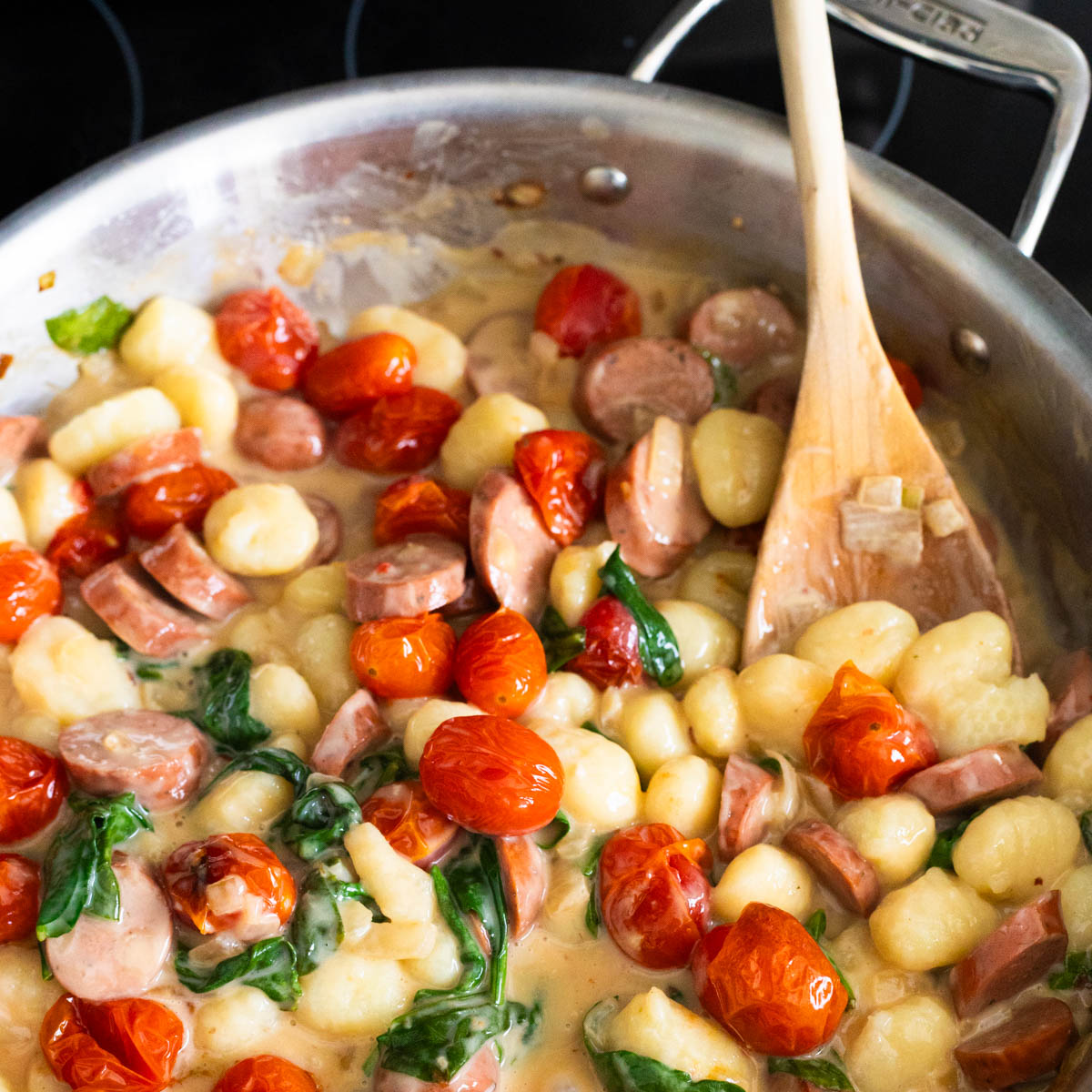 A skillet is filled with the creamy sauce coated gnocchi with roasted cherry tomatoes and wilted baby spinach.