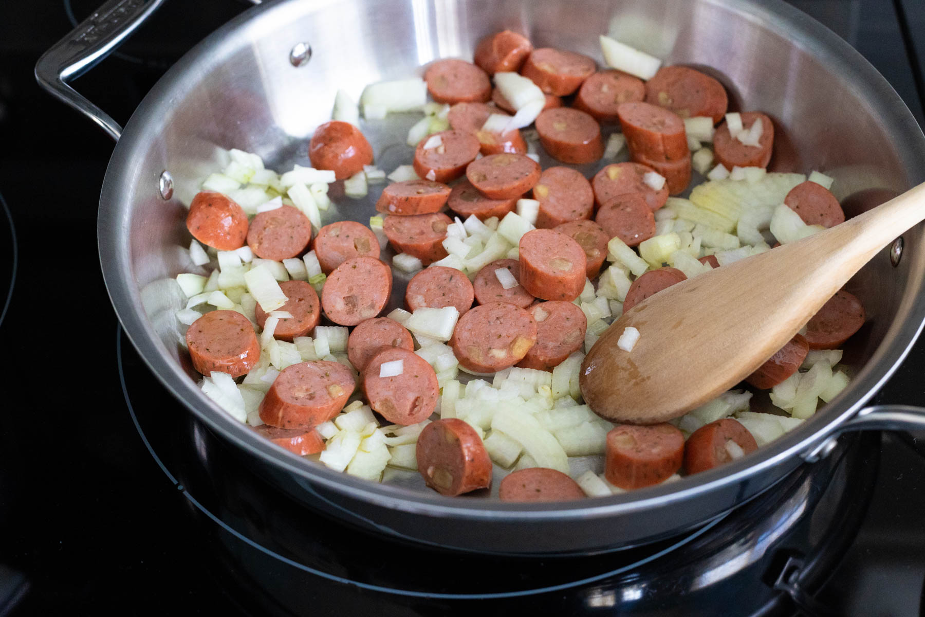 The sliced chicken sausage and chopped onions are browning in a large skillet.