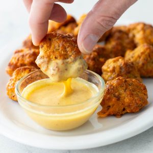 A hand dunks a sausage ball into a small cup of honey mustard dip.
