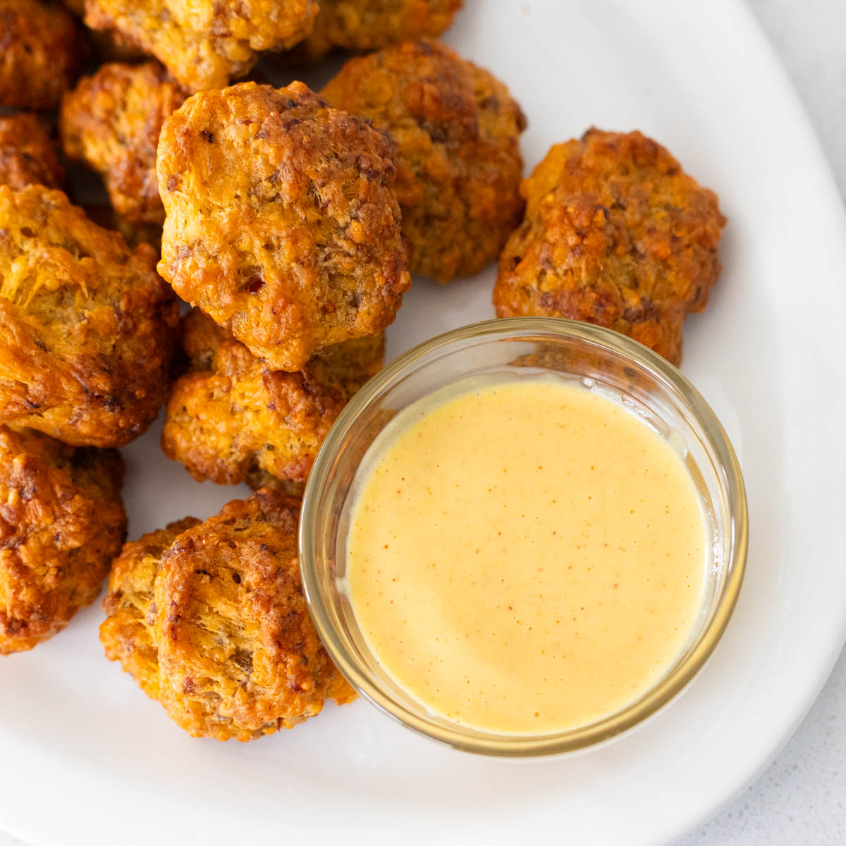 The small cup of honey mustard dip is set on a platter of homemade sausage balls.