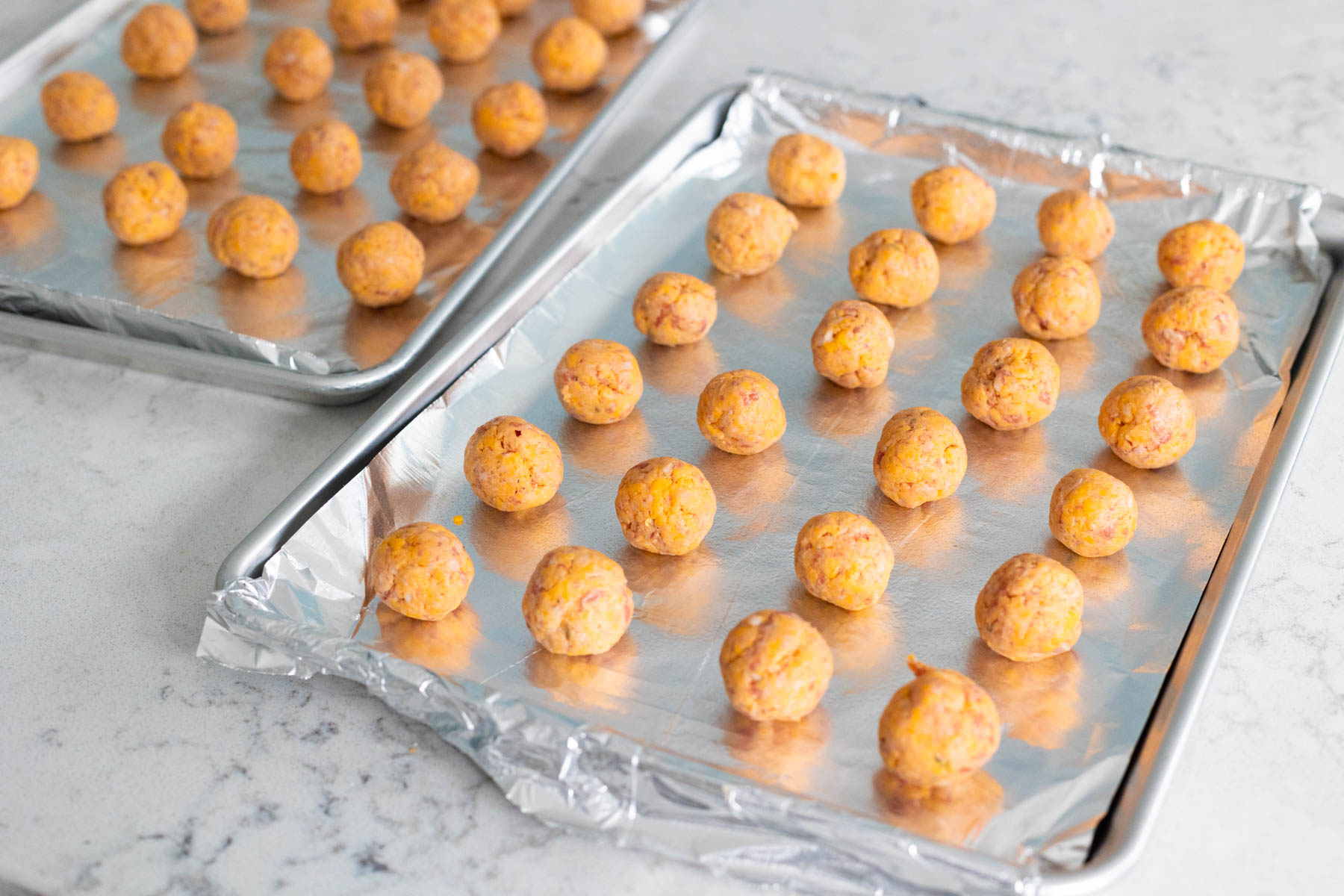 The baking pans have been lined with aluminum foil and the sausage balls are lined up in neat rows.