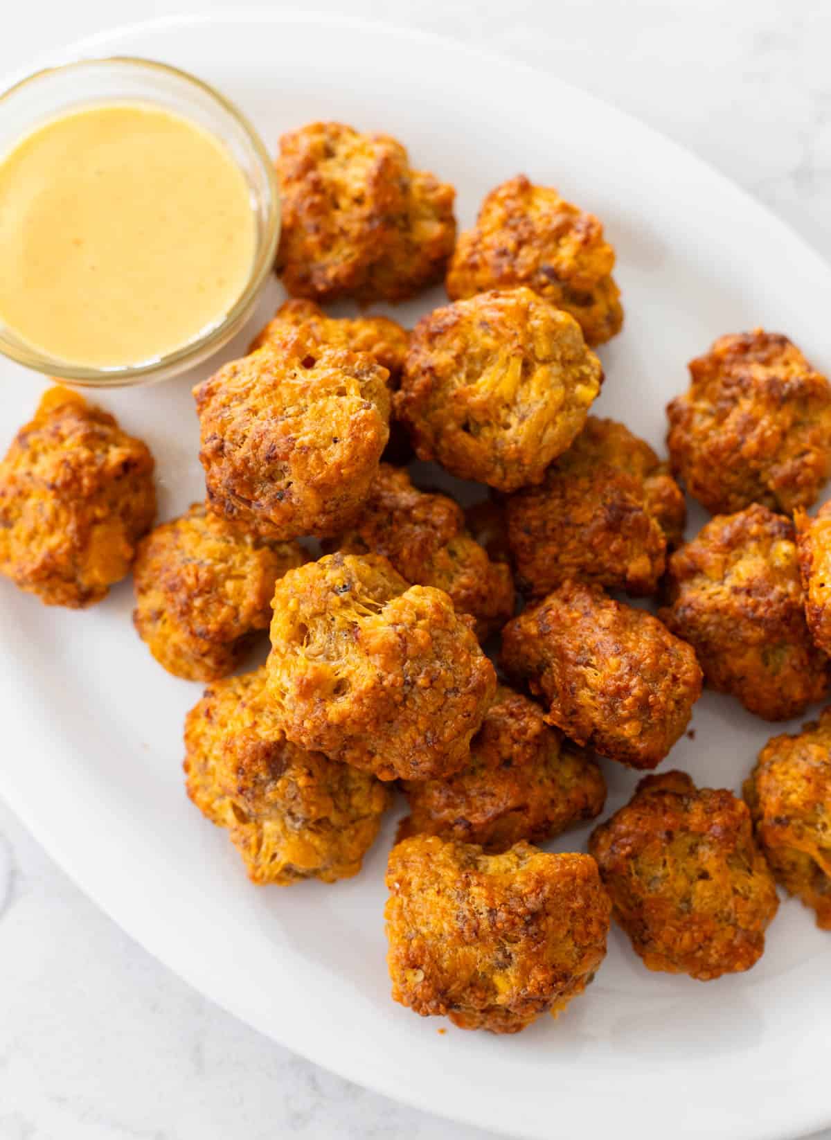 A white platter filled with Bisquick Sausage Balls and a honey mustard dip cup.