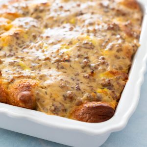 A baking dish is filled with an egg casserole that has sausage gravy over the top. Golden brown biscuits peek out from the corners.