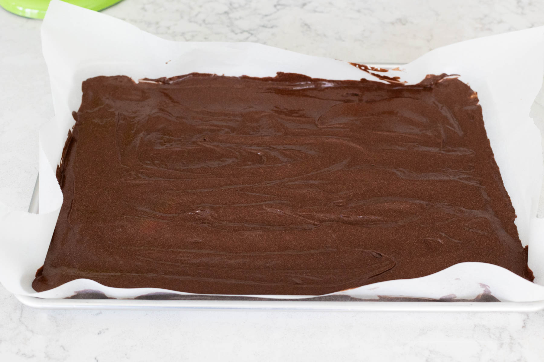 The chocolate cake batter has been spread into a large baking sheet lined with parchment paper.