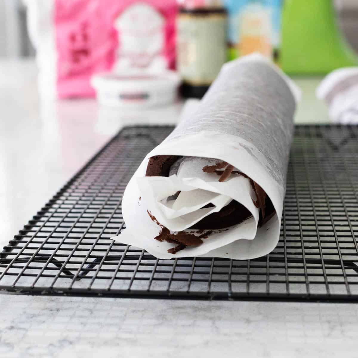 The chocolate sponge cake has been rolled with the parchment paper and is cooling on a rack.