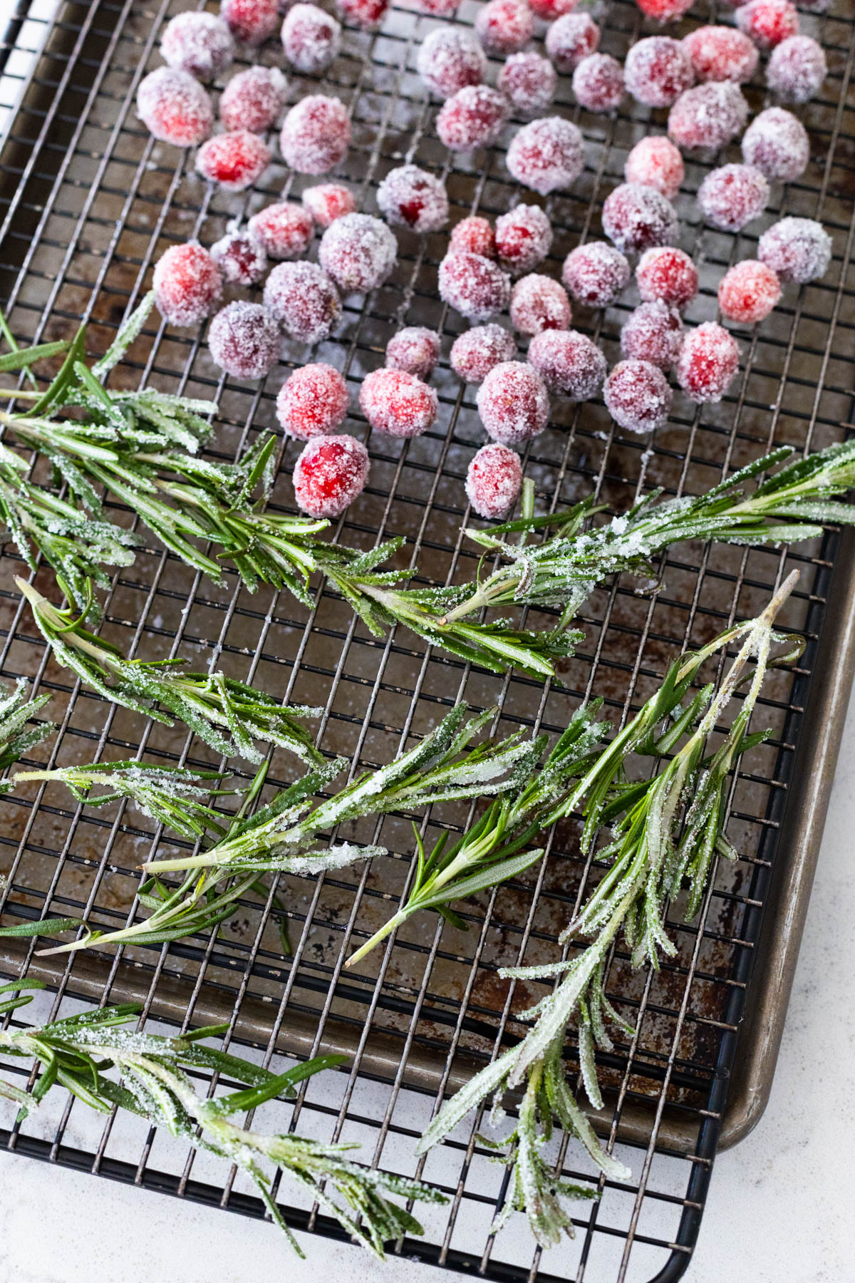 The sugared rosemary and cranberries are drying on a wire rack.