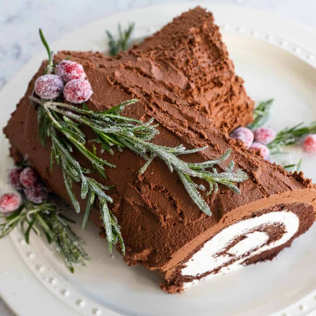 A yule log cake is decorated with fresh rosemary and sugared cranberries.