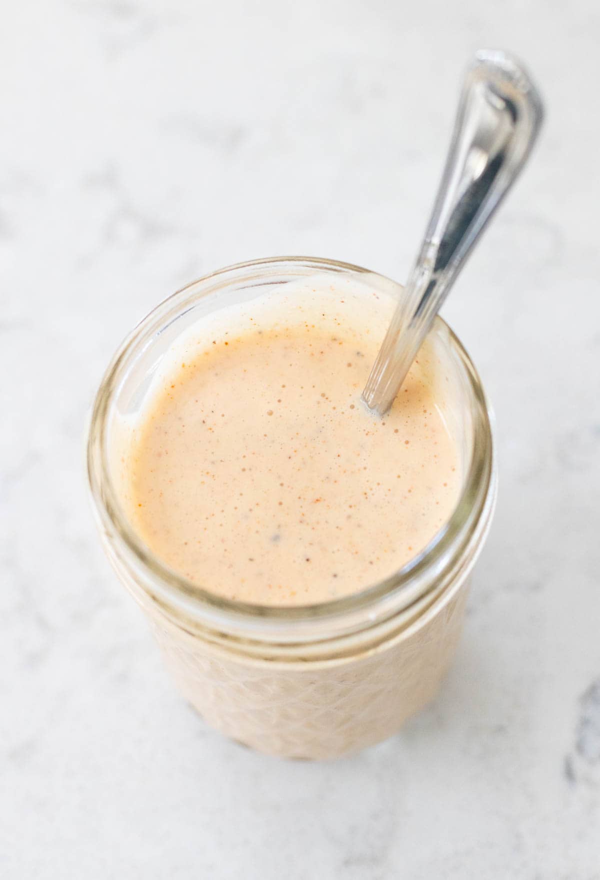 A mason jar filled with creamy Alabama white sauce has a spoon sticking out.