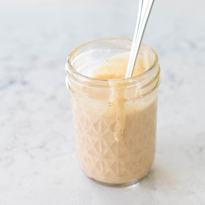 A mason jar is filled with the homemade Alabama white sauce. A drizzle is dripping down the side of the jar.