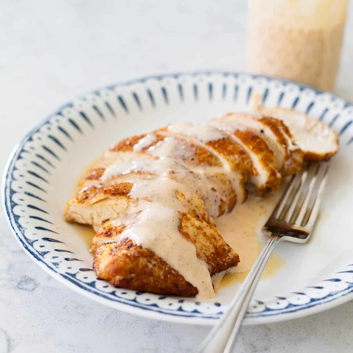 A plate with sliced barbecue chicken has a drizzle of Alabama bbq white sauce over the top.