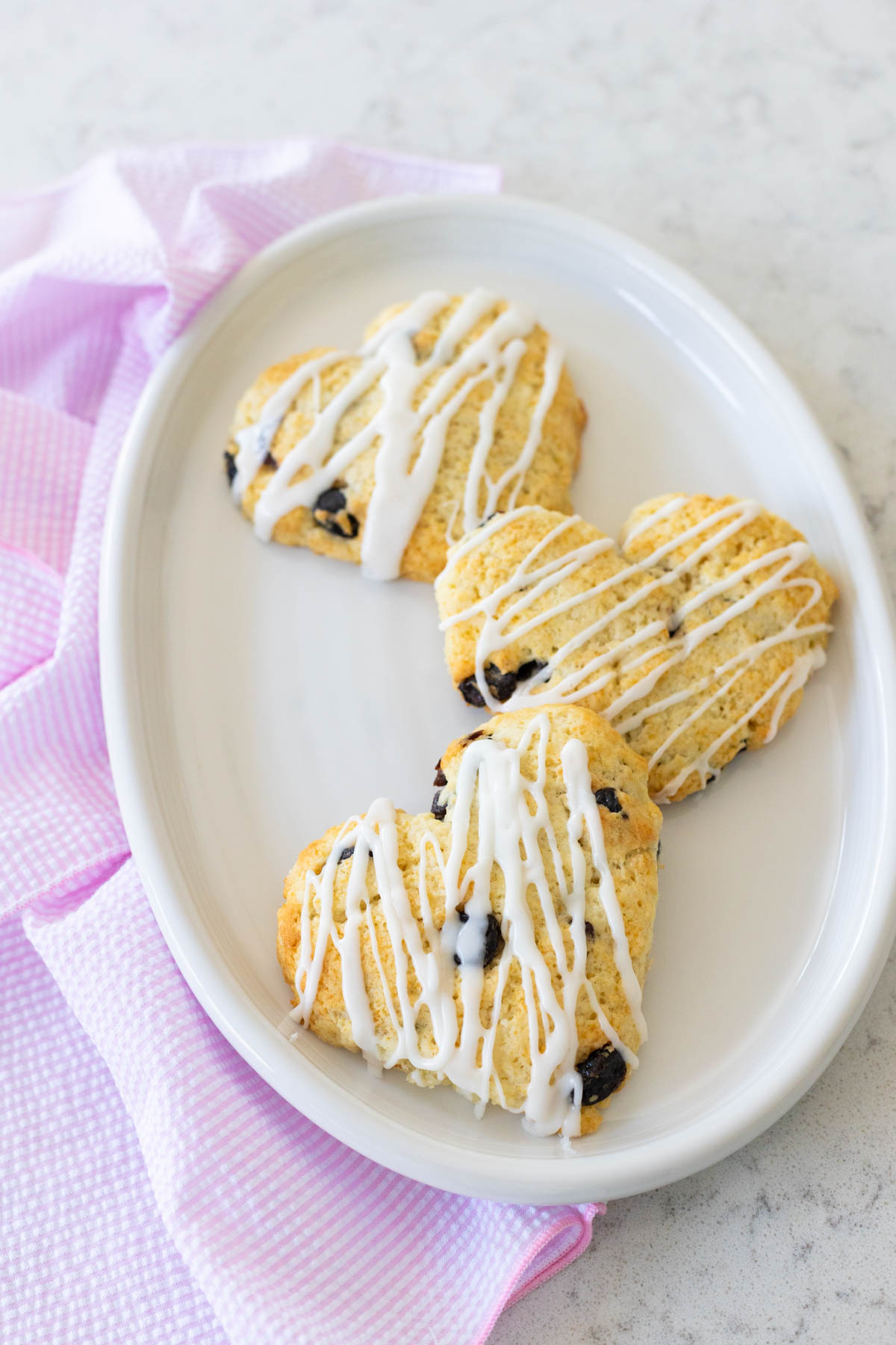 A white platter has 3 heart-shaped almond cherry scones with an almond icing drizzle.