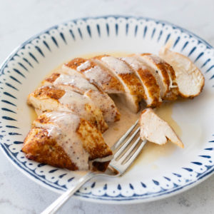 A plate of sliced chicken has a white BBQ sauce drizzled over the top.