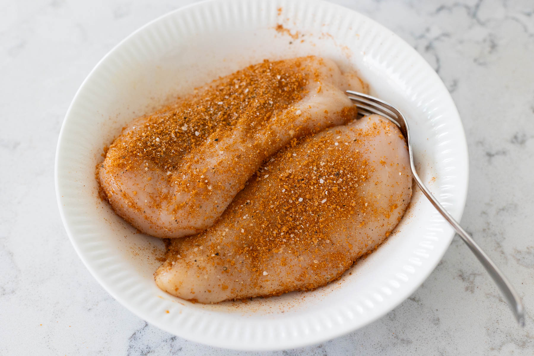 The chicken breasts in the mixing bowl have been coated with the dry rub.