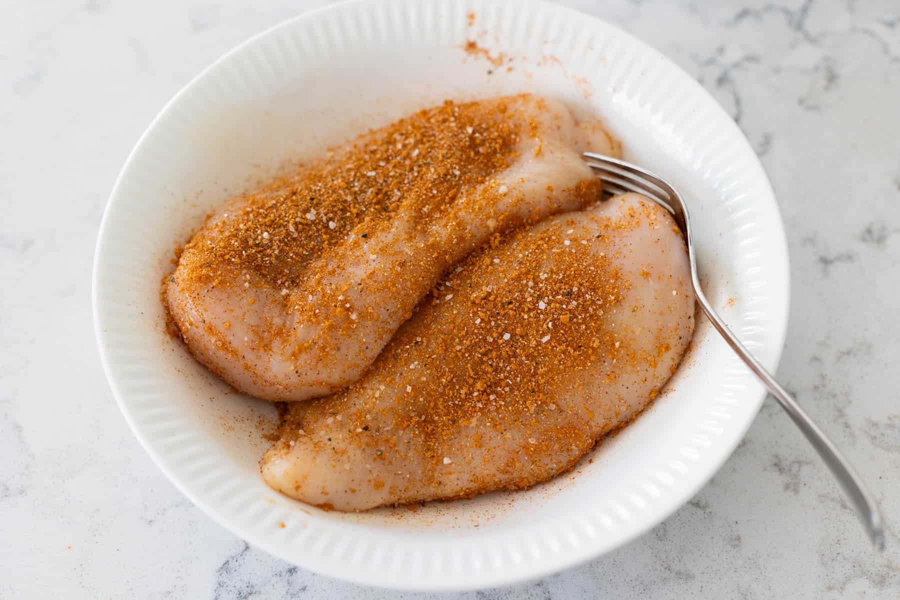 The chicken breasts in the mixing bowl have been coated with the dry rub. 