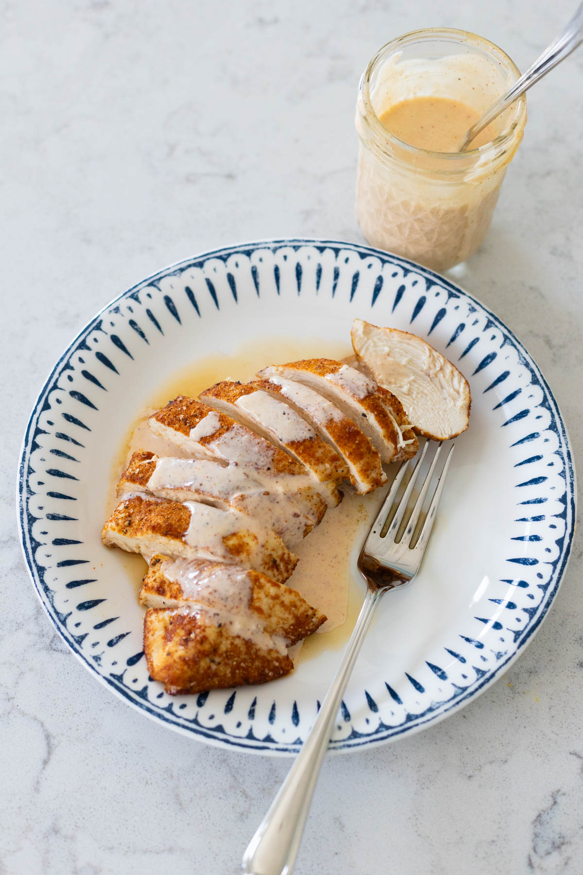 The baked chicken breast has been sliced and served on a plate with a drizzle of Alabama white sauce.