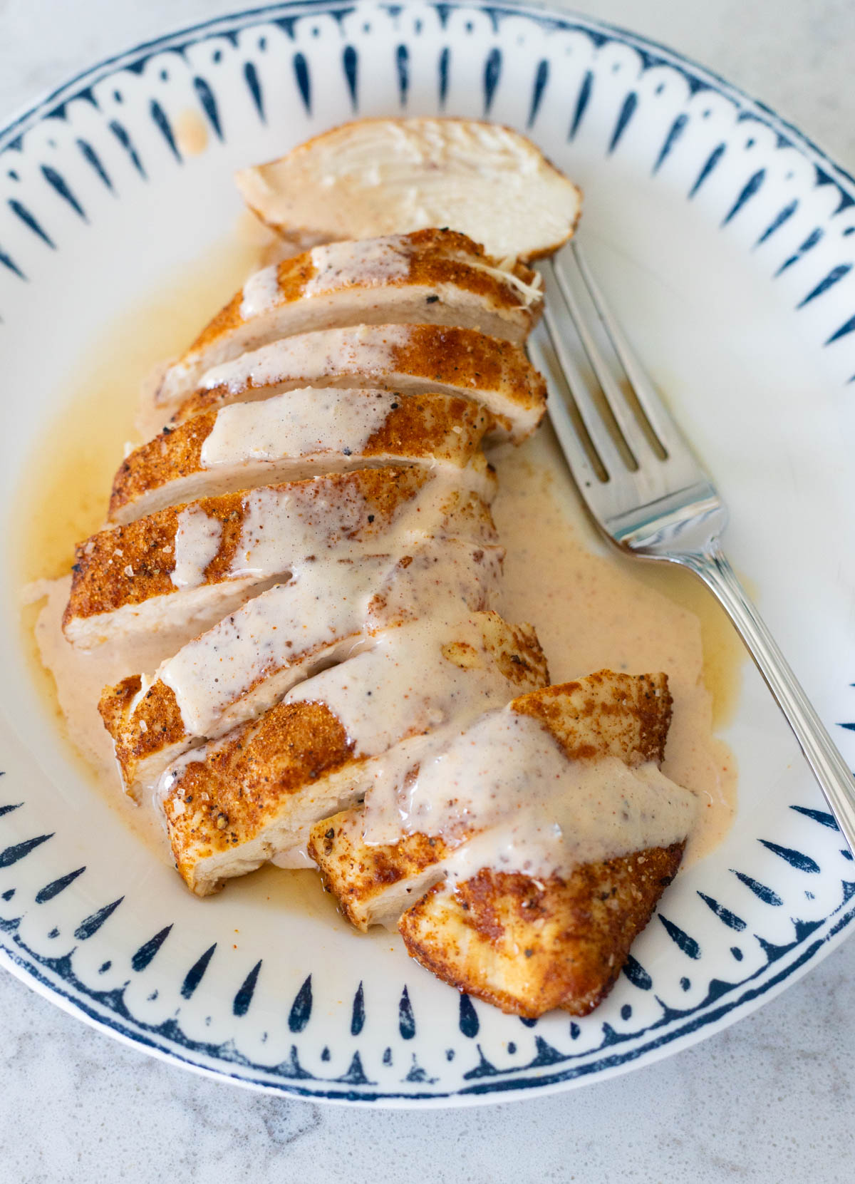 A blue and white plate has sliced chicken breast with a drizzle of Alabama white bbq sauce over the top.