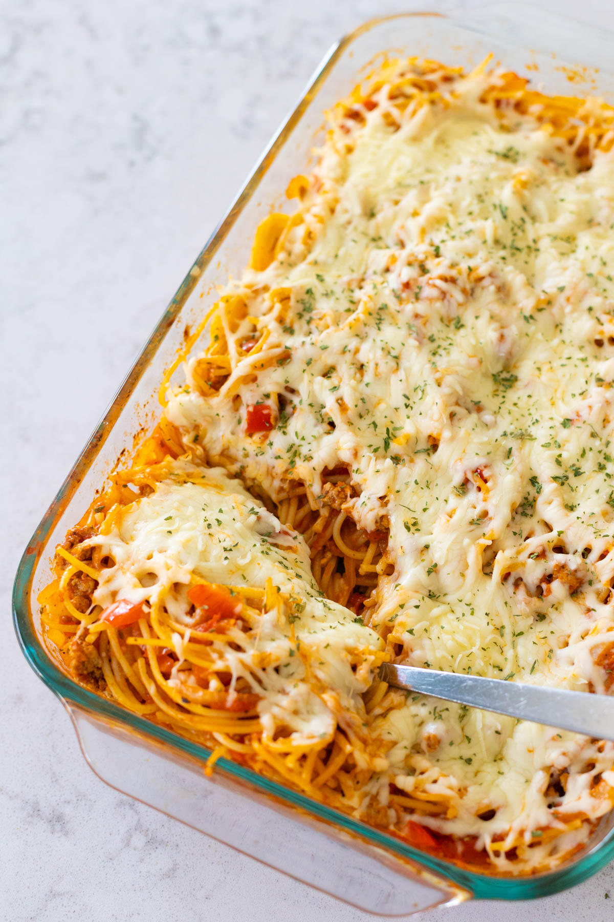 A baking dish filled with baked spaghetti topped with shredded cheese.