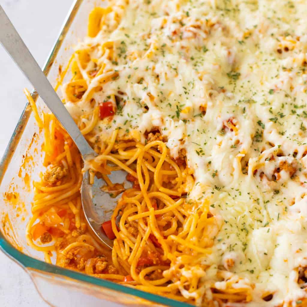 A pan of baked spaghetti has a spoon serving up a portion from the corner.