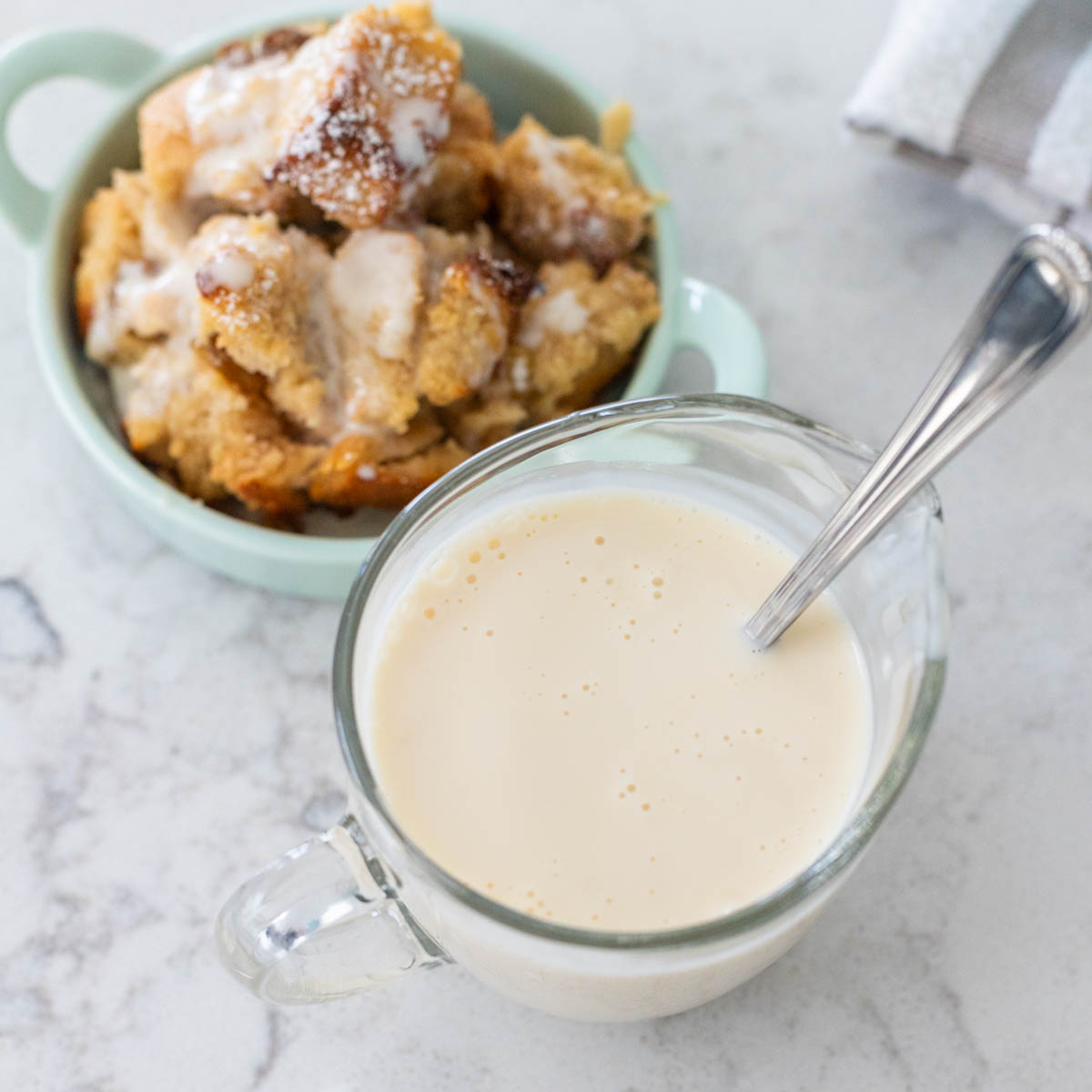 The pitcher of bourbon sauce sits next to a small dish of bread pudding.