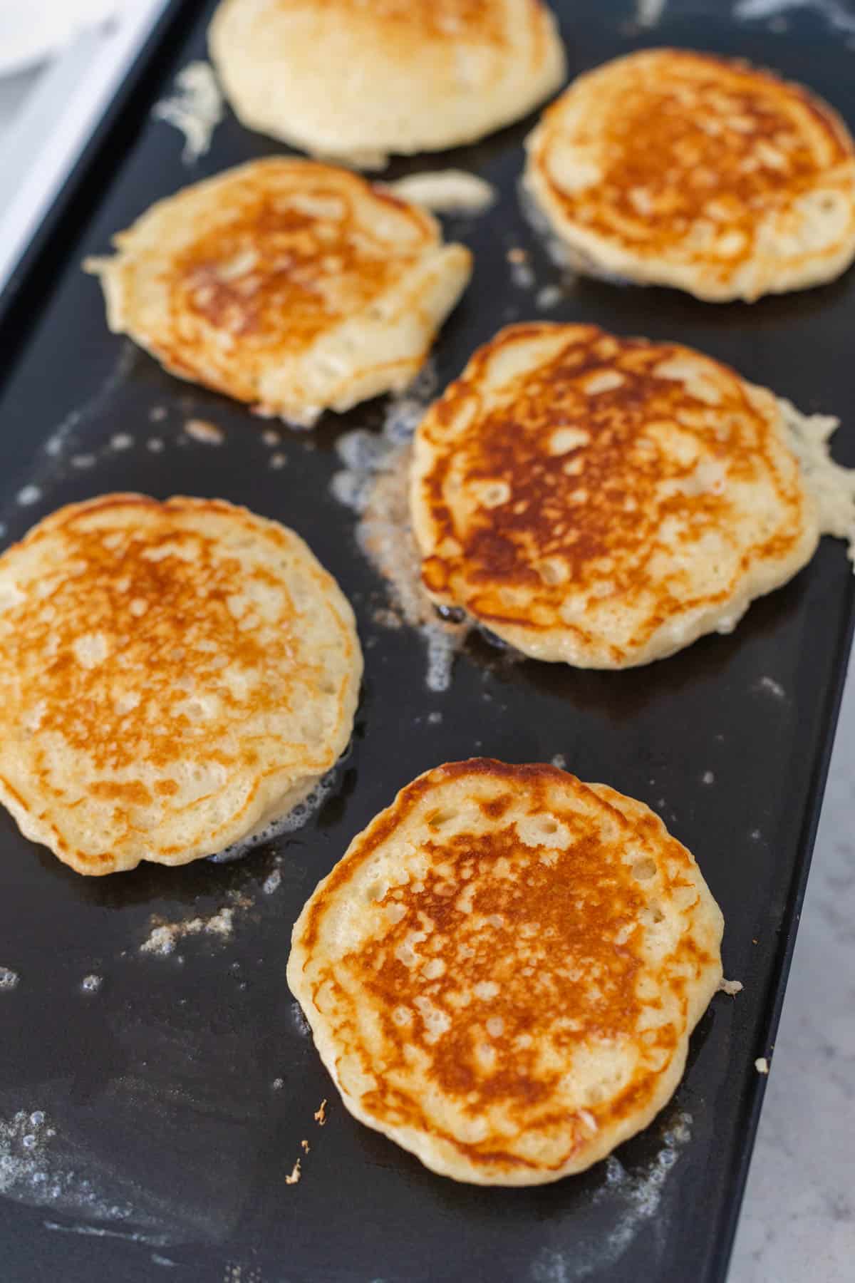 The pancakes are still on the griddle but have been flipped.