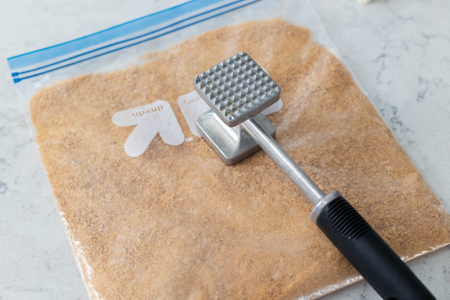 The graham crackers have been crushed in a plastic bag with a kitchen mallet.