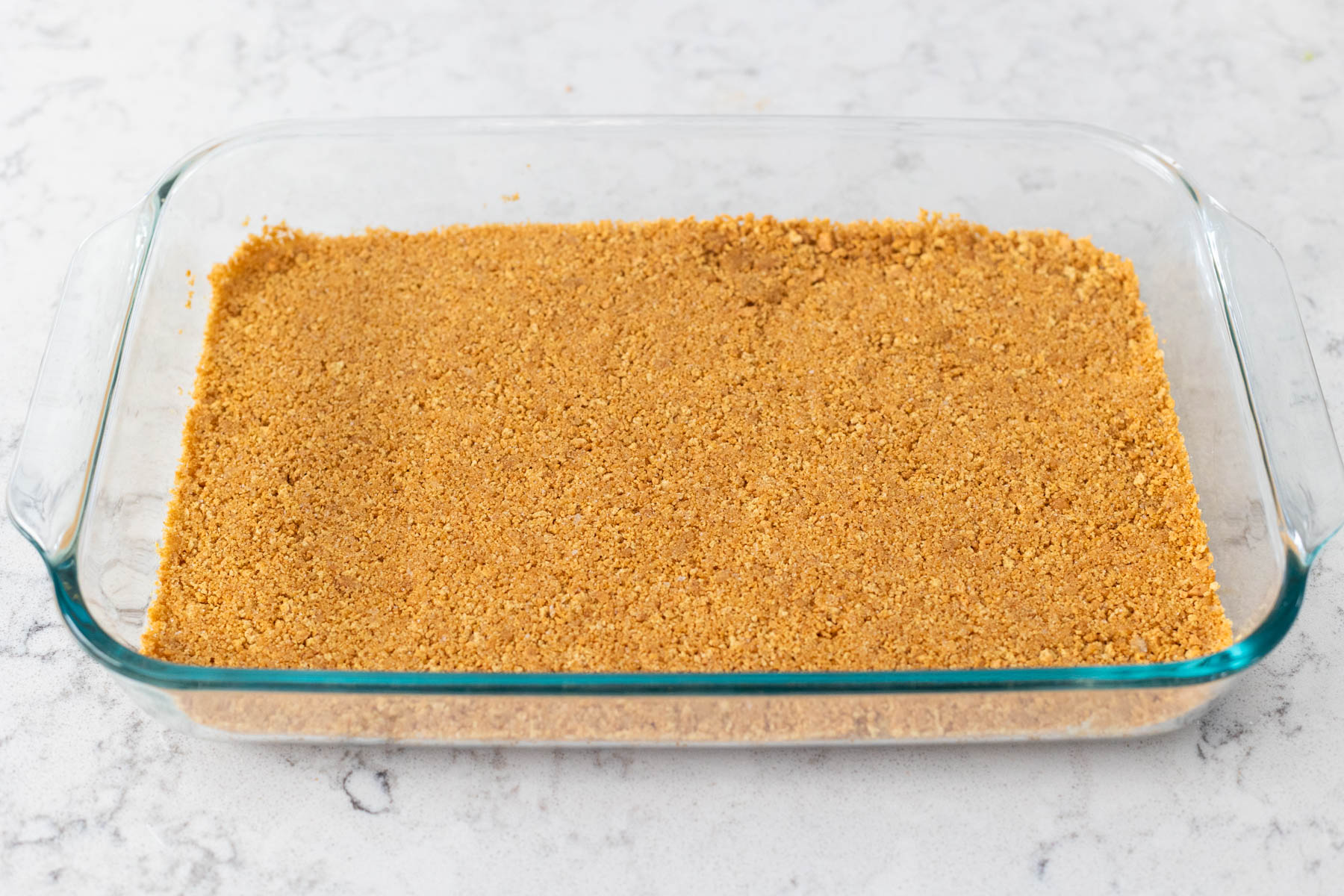 A baking dish is filled with a graham cracker crust.