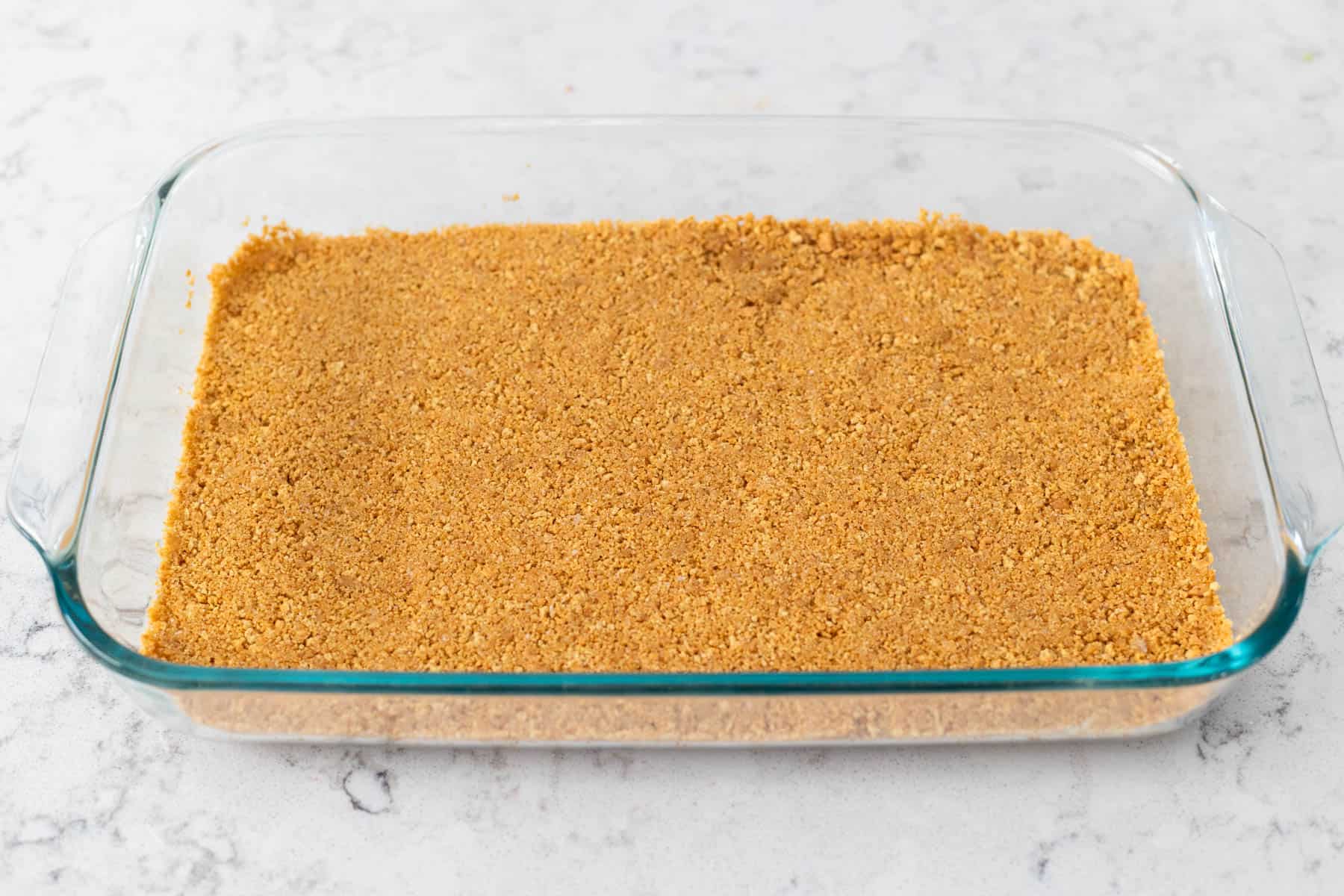 A baking dish is filled with a graham cracker crust.