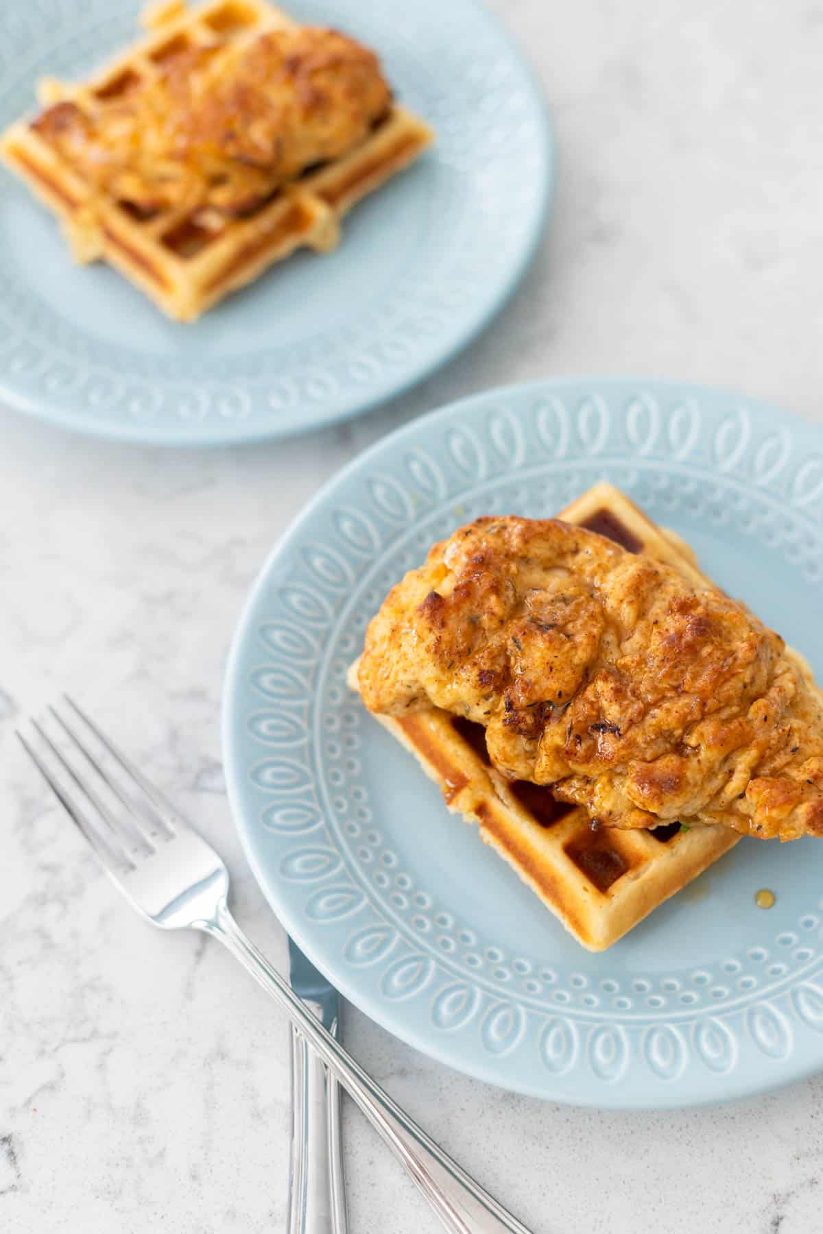 Two plates of chicken and waffles with a fork.